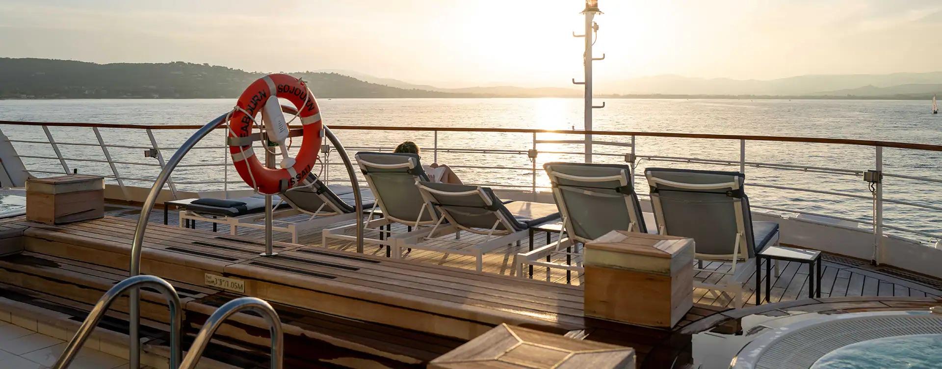 Loungers on the open deck of a cruise ship at sea, with the horizon beyond.