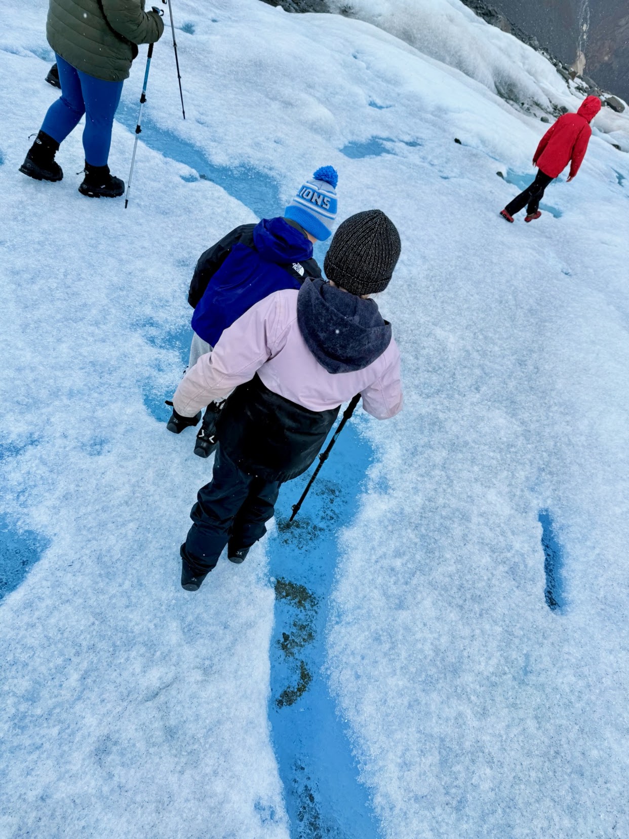 Two children walking across the blue and white surface of a glacier