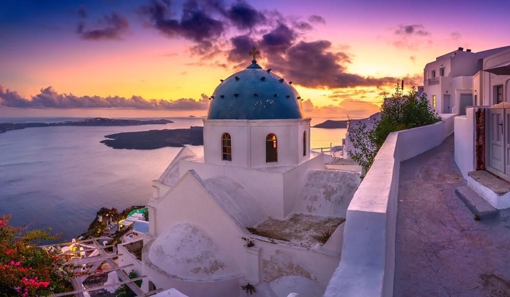 A blue-domed church above the caldera at sunset in Santorini