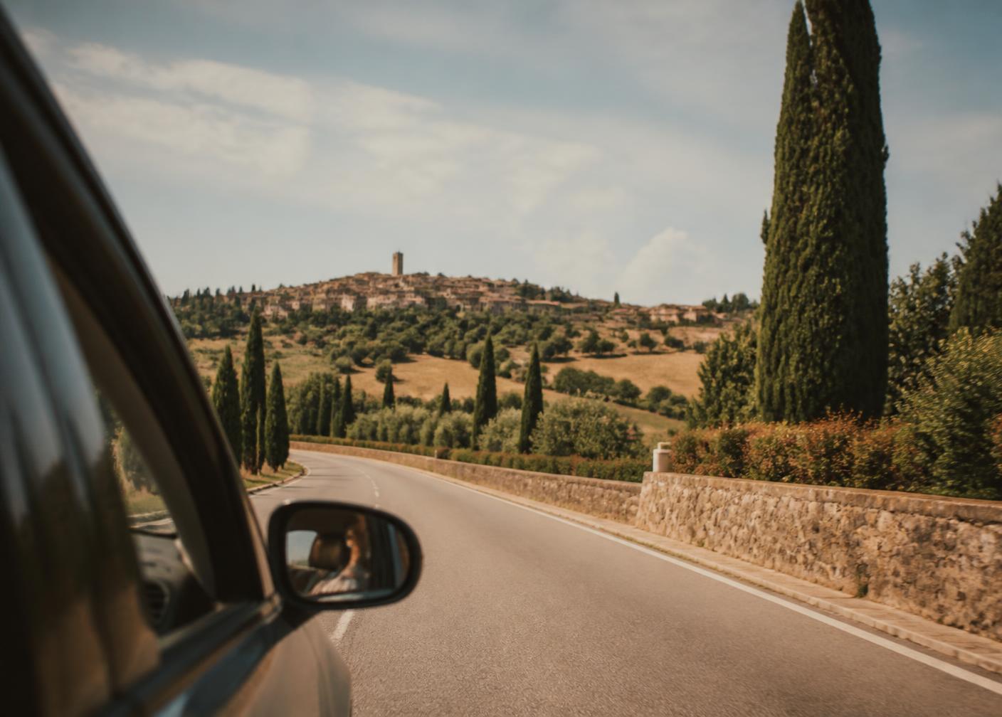 A Tuscan hill town and cypress trees seen from the window of a private car